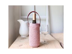 a wine bottle in a crocheted pink basket next to a glass of wine