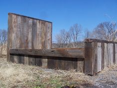 an old wooden bench sitting in the middle of a dry grass field next to trees