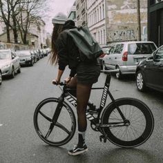 a woman riding a bike down a street next to tall buildings and parked cars on both sides