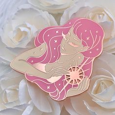 a pink and gold pin with an image of a mermaid sitting on top of it