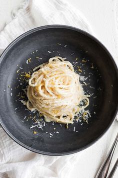 a black bowl filled with spaghetti and parmesan cheese