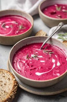 two bowls of beet soup with bread on the side