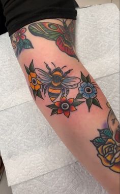 a woman's arm with tattoos on it and a bee sitting on the flower