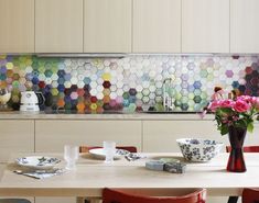 a table with plates and cups on it in front of a colorful tile backsplash