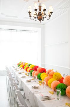 a long table with many different colored paper balls on it and place settings for the tables