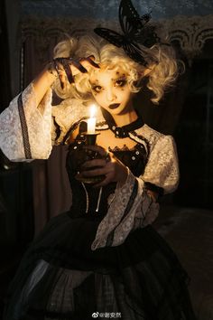 a woman holding a lit candle in her hand and wearing a black dress with white laces