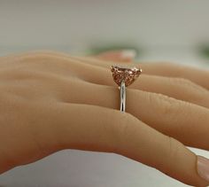 a woman's hand holding a ring with a pink diamond on the middle of it