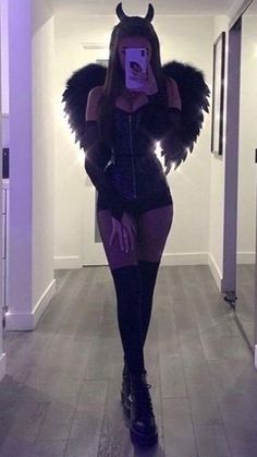 a woman in a devil costume taking a selfie with her cell phone while walking down the hallway