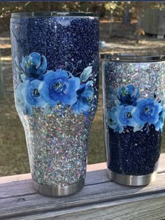 two tumbles with blue flowers painted on them sitting on a wooden table outside in the sun