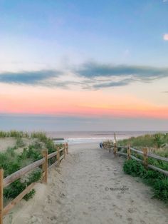 a wooden fence on the beach with grass and sand in front of it at sunset