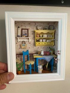 a hand holding up a miniature dollhouse with furniture in it's display case