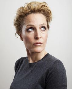 a woman with blue eyes looks up at the camera while wearing a black shirt and grey sweater