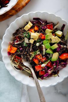 a white bowl filled with salad next to a fork