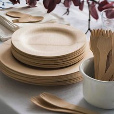 there are many wooden utensils on the table with plates and cups next to it