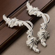 an ornate pair of silver earrings sitting on top of a wooden floor next to a window