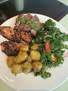 a white plate topped with meat and potatoes next to a pile of veggies