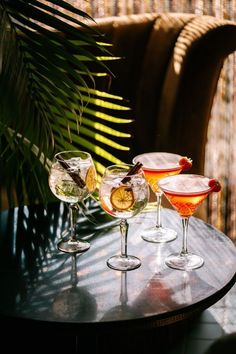 three glasses filled with different types of drinks on top of a table next to a palm tree