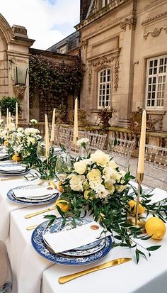 a long table with plates and place settings set up for an outdoor dinner party in front of a large building