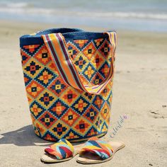 a colorful bag sitting on top of a sandy beach next to the ocean and a pair of flip flops