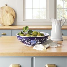 a blue and white bowl filled with fruit on top of a wooden counter next to a window