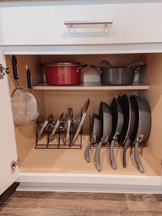 an open cabinet with pots and pans on the bottom shelf, next to other kitchen utensils