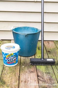 a bucket and brush sitting on a wooden deck next to a blue bucket filled with dirt