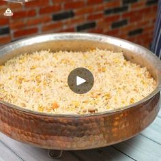 a pan filled with rice sitting on top of a wooden table next to a brick wall