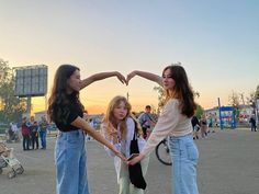 three girls standing in a parking lot making a heart shape with their hands as the sun sets