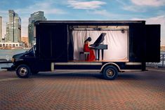 a black truck with a woman playing the piano on it's side and buildings in the background