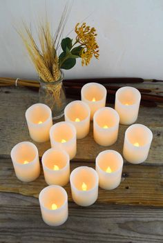 many white candles are arranged on a wooden table next to a vase with yellow flowers