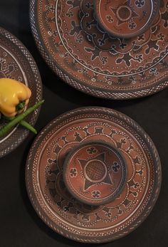 three brown plates with decorative designs and yellow peppers in them on a black tablecloth