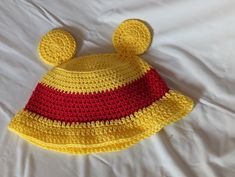 a crocheted yellow and red hat laying on top of a white bed sheet