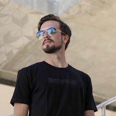 a man with sunglasses on standing in front of a building and looking off into the distance