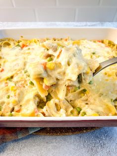 a casserole dish filled with chicken, vegetables and cheese is being spooned