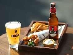 there is a beer and some food on the wooden table with it's tray