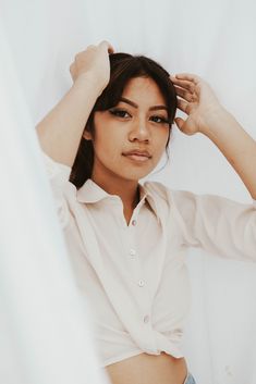 a woman is posing with her hands on her head while wearing a white shirt and jeans