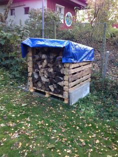 a pile of wood sitting in the grass next to a building with a blue tarp over it