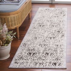 a white rug with black and grey designs on the floor next to a plant in a pot