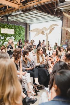 a group of women sitting next to each other in front of a crowd at a fashion show