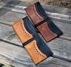 two leather wallets sitting on top of a wooden table next to each other with holes in them