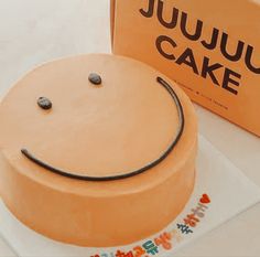 a smiley face cake sitting on top of a table next to a box with the name jujuu cake written on it