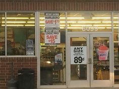 a store front with many signs on the glass doors and one has a black trash can in front of it