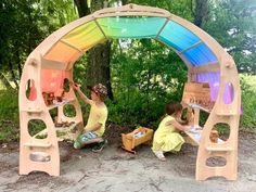 two children are playing in an outdoor play area made out of plastic bottles and cardboard boxes