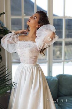 a woman in a white dress standing next to a window