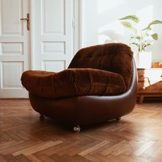 a brown chair sitting on top of a wooden floor next to a potted plant