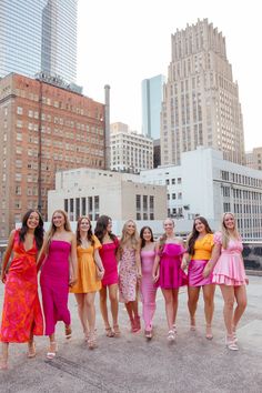 a group of women standing next to each other on top of a cement ground in front of tall buildings