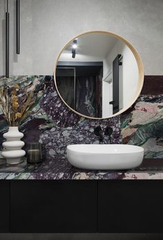 a bathroom with marble counter tops and a round mirror on the wall next to it