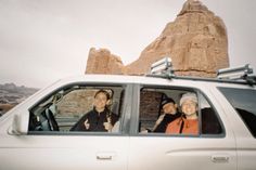 two women sitting in the passenger seat of a white car with mountains in the background