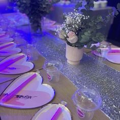 the table is set with pink and white plates, silverware, and vases