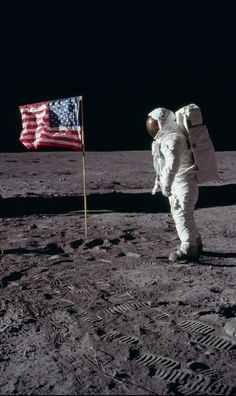 an astronaut standing on the moon next to a flag and looking down at the ground